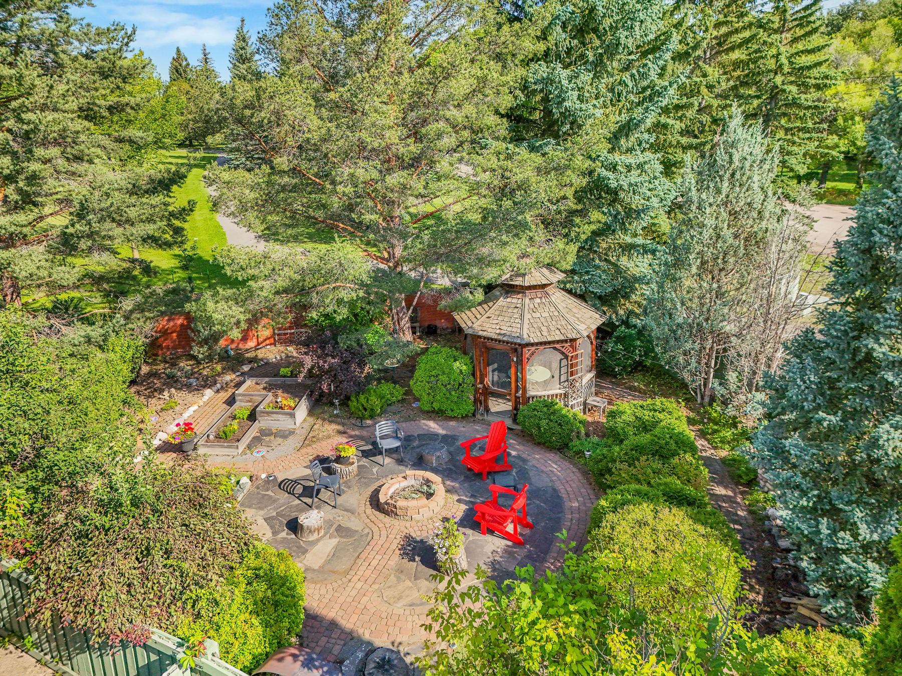 Aerial view down over the back garden — the flagstone fire pit terrace, the gazebo and the raised beds under mature trees.