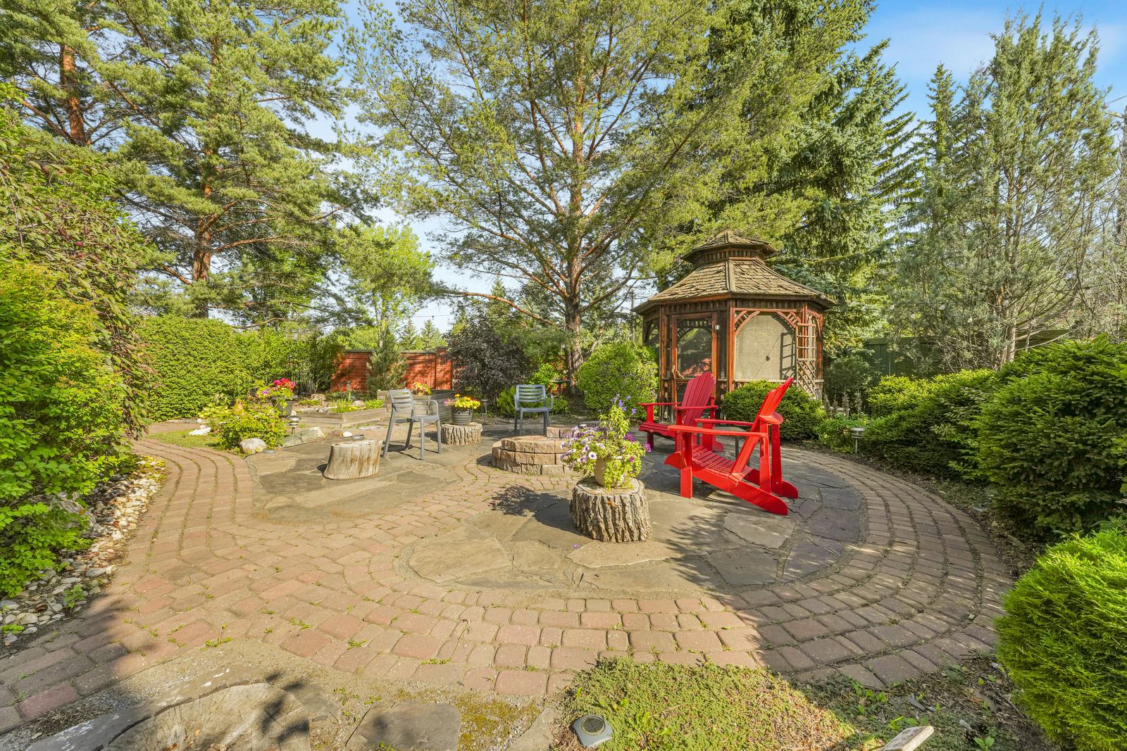 The flagstone fire pit terrace in daylight, laid in circles with red chairs and the gazebo behind.