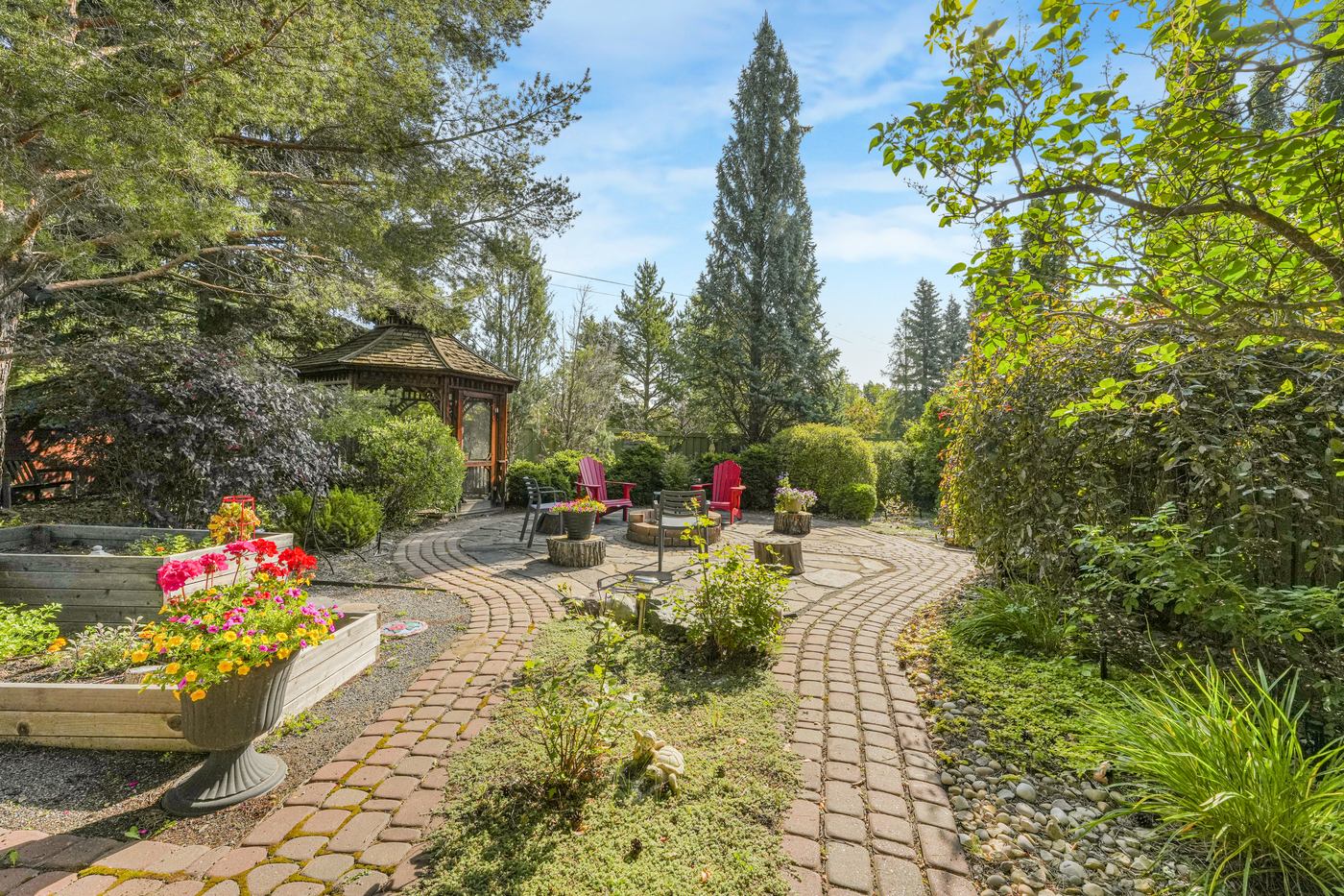 Raised garden beds in flower and curved stone paths winding through planted borders toward the gazebo.