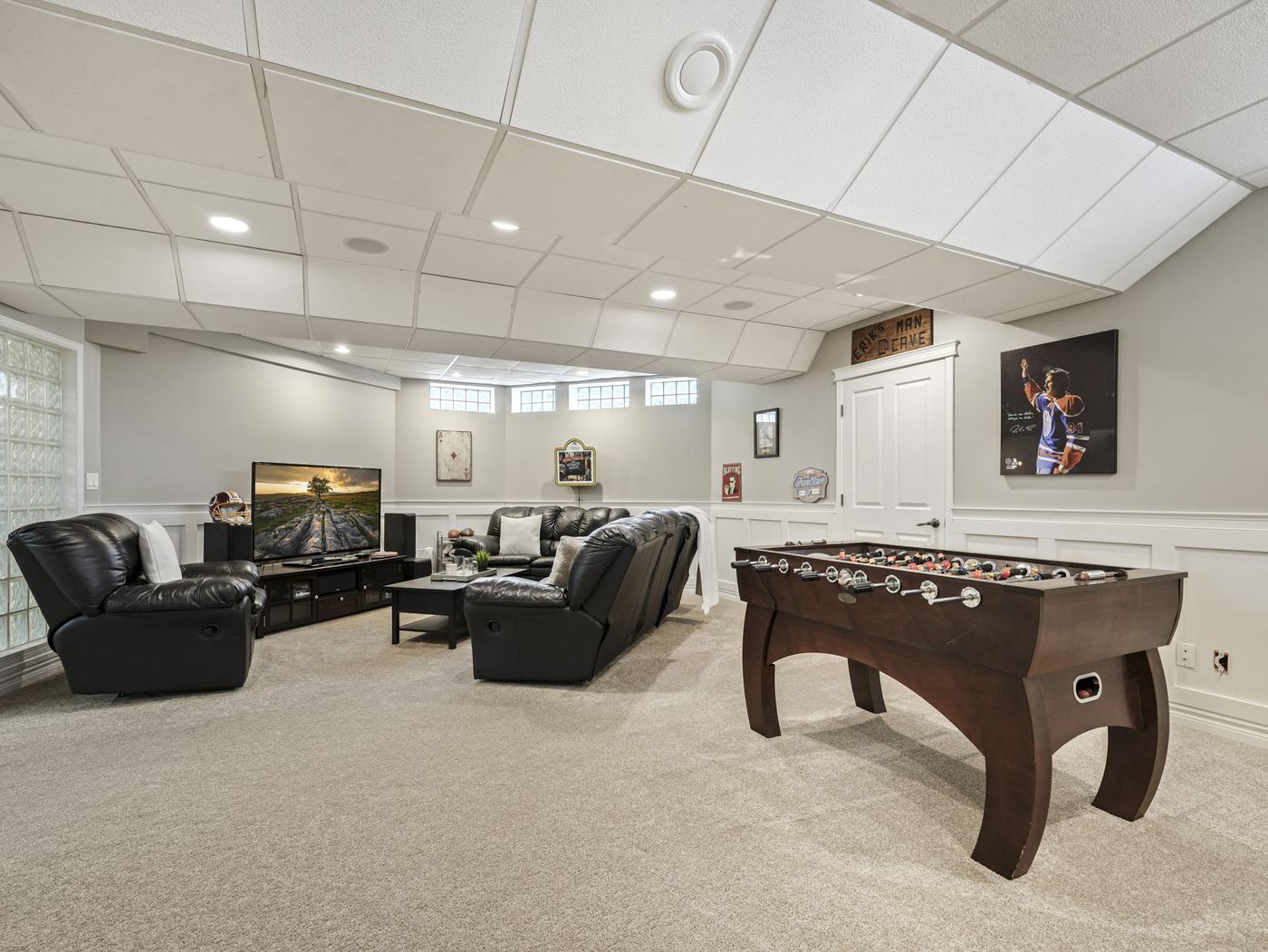 The finished lower level recreation room with seating, a games table and glass block windows.
