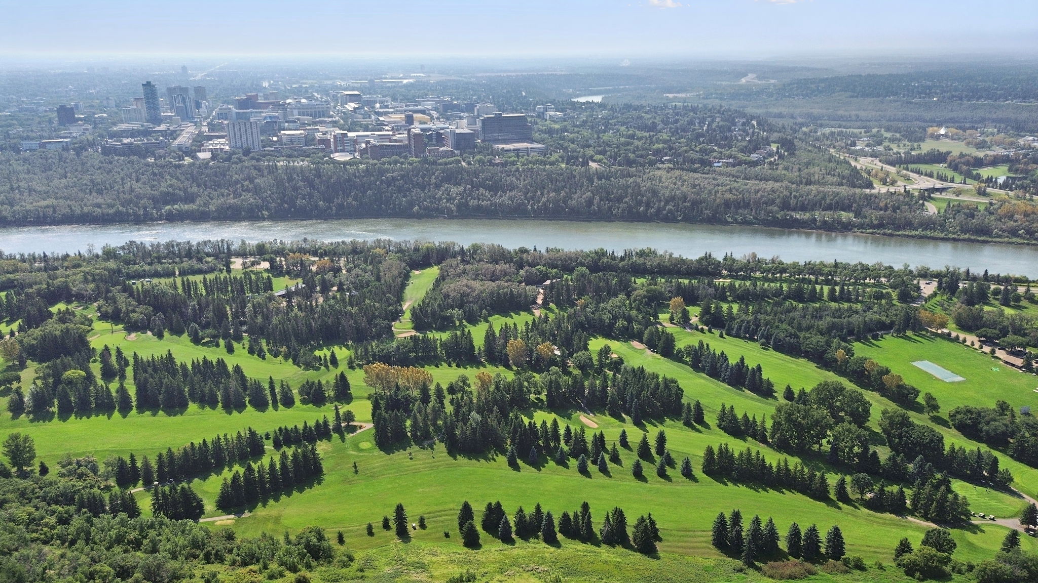 Aerial view of the North Saskatchewan River valley and the Victoria Golf Course in summer, the downtown high-rises on the far bank.