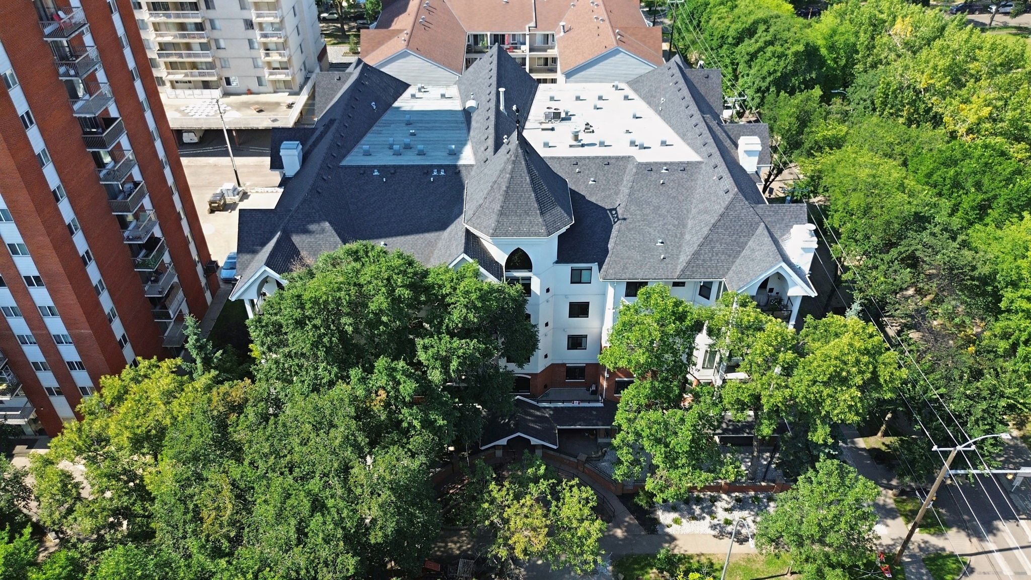 Aerial view down onto The Wesley's roof and the mature trees along 117 Street, the neighbouring high-rise to the left.