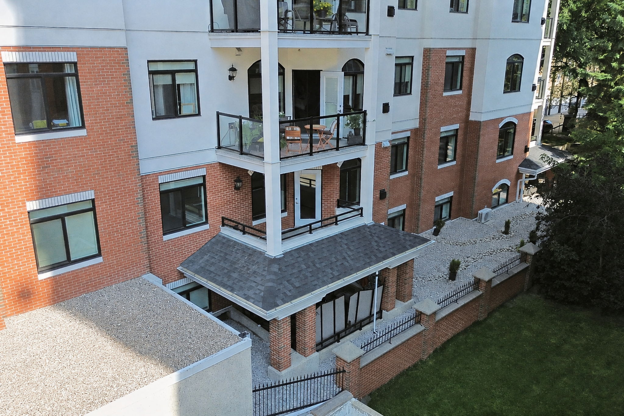 Looking down the brick and stucco face of The Wesley at the stacked covered balconies, their new railings and deck surfaces, and the landscaped entry below.