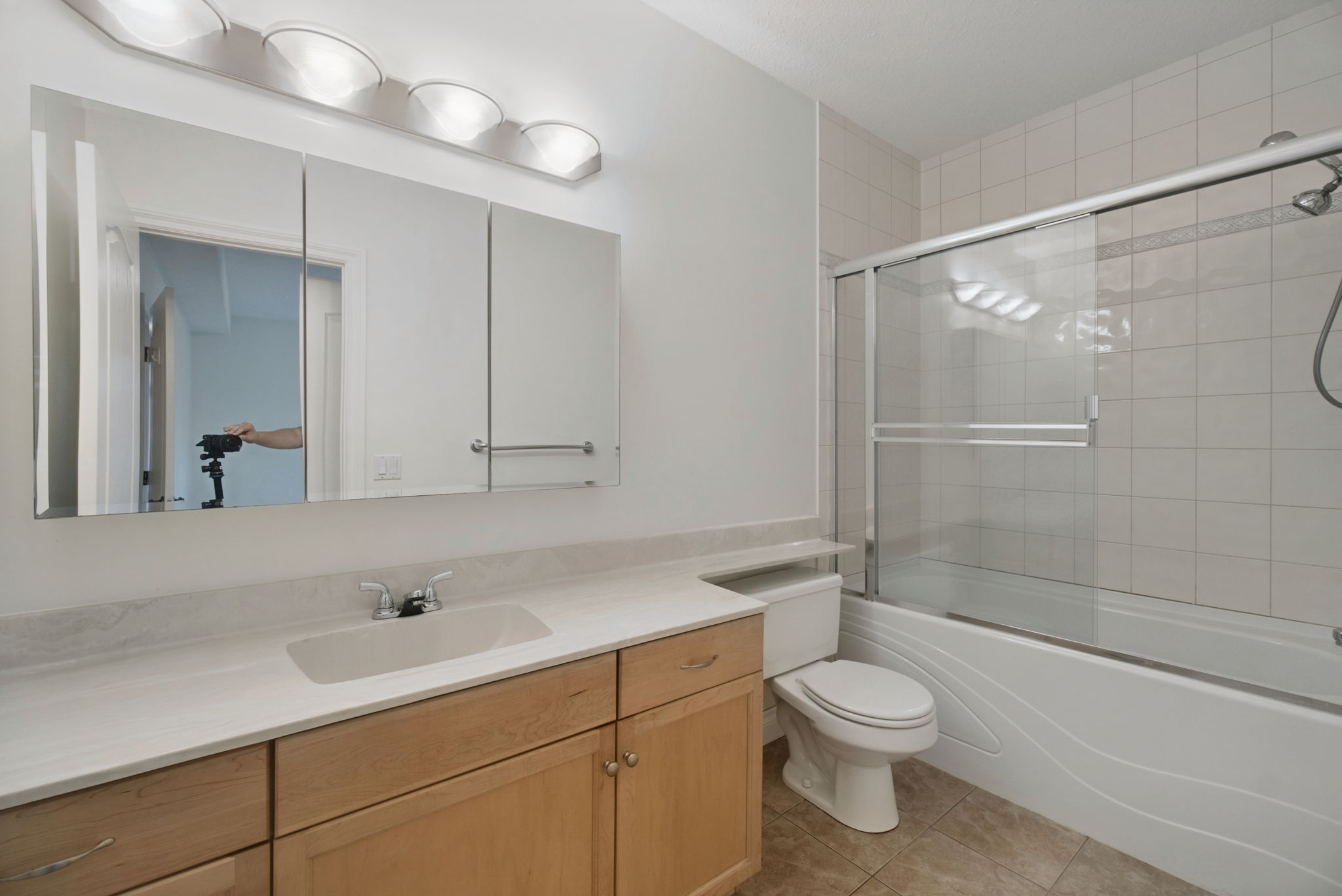 The second full bathroom with a maple vanity, a lit mirror and a tub with a glass shower door.