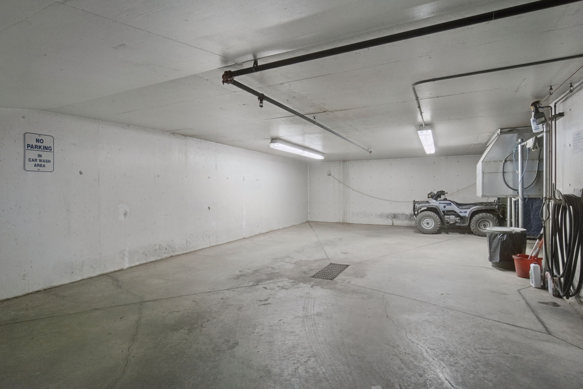 The car wash bay inside the parkade, a lit concrete bay with a hose reel and floor drain.