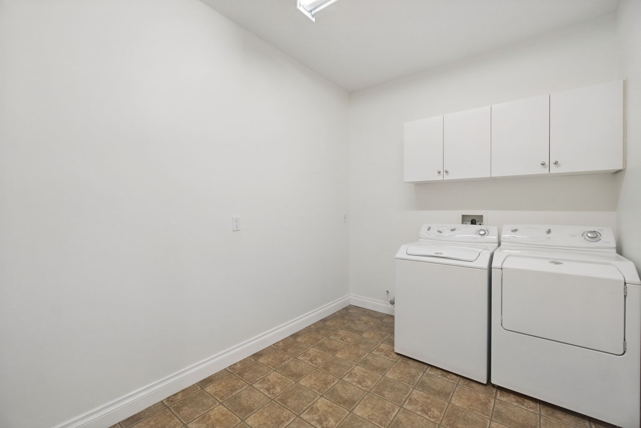 The laundry room with a full-size washer and dryer under a row of white cabinets.