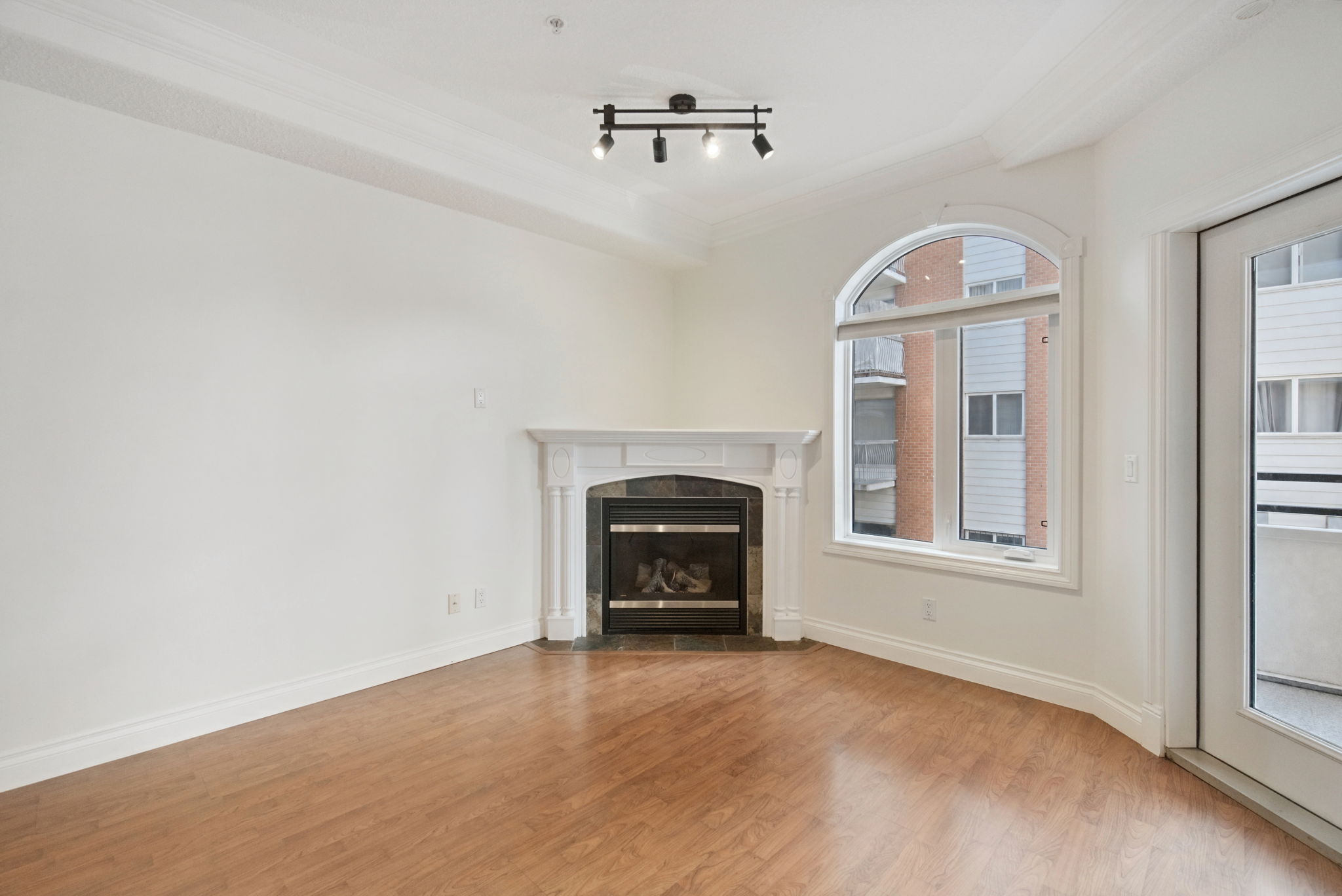 The corner gas fireplace with a white mantel and tile surround, beside the arched window and the door out to the balcony.