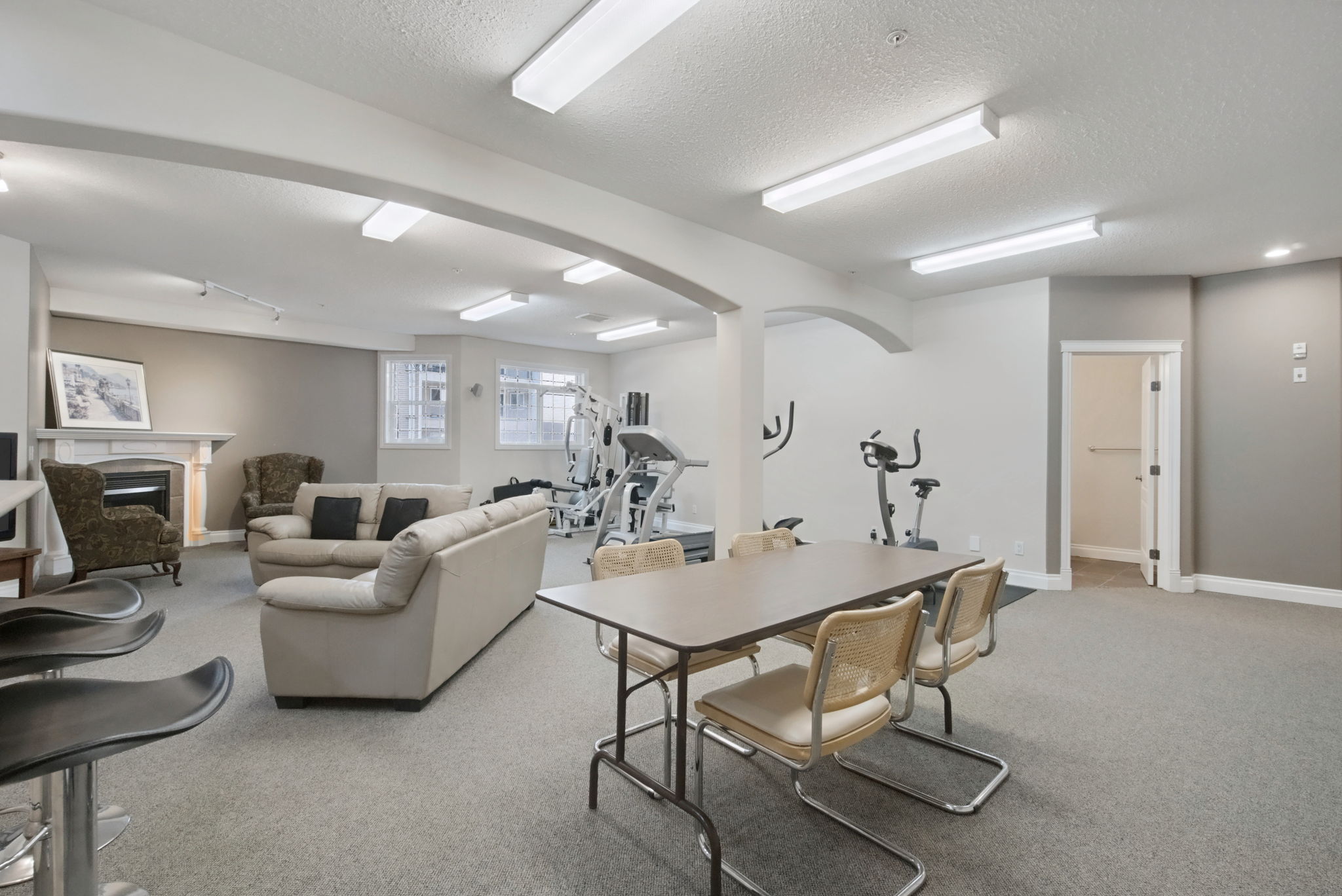 The social room, a large carpeted space with sofas, folding tables and a kitchen along one wall under arched openings.
